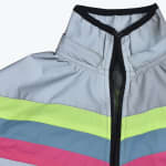 Close-up of a reflective silver jacket featuring a high collar with black trim, a partially unzipped black zipper, and horizontal stripes of neon yellow, blue, and pink.