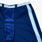 Close-up of dark blue athletic pants with a white waistband, blue belt loops, a shiny blue front panel, and a white side stripe.