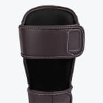 Close-up view of a dark brown leather shin guard upper strap with white stitching and a black inner lining against a white background.