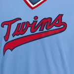 Close-up of a light blue Minnesota Twins baseball jersey featuring the red script Twins logo with a dark blue outline.
