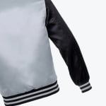 Close-up view of a light gray varsity jacket with a black sleeve and black and white striped ribbed cuffs and hem.