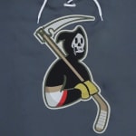 An embroidered patch on a grey hoodie featuring a cartoon Grim Reaper holding a scythe that is also a hockey stick.