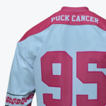 Back view of a white hockey jersey with pink shoulders reading PUCK CANCER and a large pink number 95.