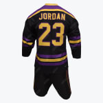Based on the design style of the uniform, here is a corrected description: Back view of a custom black sports jersey with "JORDAN" and the number "23" in purple with gold trim, featuring purple and gold stripes on the V-neck collar and sleeve cuffs. It is paired with matching black shorts that feature purple and gold trim, displayed on a white mannequin against a plain white background.