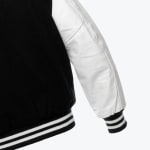 Close-up of a varsity jacket with a black wool body, a white leather sleeve, and black and white striped ribbed cuffs and hem.