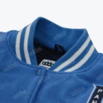 Close-up of a blue varsity jacket collar with white stripes and a snap button, showing the Adidas brand tag inside.