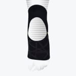 A black compression knee sleeve with an open patella cutout and a geometric criss-cross support pattern on the lower half, displayed against a white background with stylized fading line graphics.