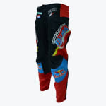 A pair of black, red, and blue motocross pants featuring various sponsor logos like Red Bull and Fox, shown standing upright against a white background.