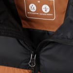 Close-up of a black and brown jacket with a brown inner label showing size M, water-resistant, and isotherm warmth features next to a zipper.