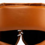 Close-up view of the padded forehead section of a brown leather boxing headguard, showing the fine leather texture, stitching, and a glimpse of the lace-up closure.