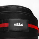 Close-up of a black weightlifting belt with a red stripe and a rectangular patch displaying the white addos brand logo.