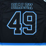 The back of a black sports jersey with the name BIALEK and the number 49 in black block font outlined in blue and white.