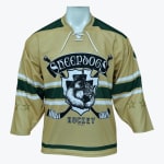 A gold hockey jersey with green and white stripes, featuring a central logo of a sheepdog wearing a hat inside a shield with crossed hockey sticks and the text Sheepdogs Hockey.