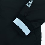Close-up of a black jacket sleeve showing a ribbed black cuff with a thick white stripe and a partial white star logo on the upper sleeve.