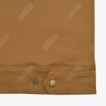 Close-up of a brown canvas jacket adjustable hem tab with a brass snap button.