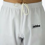 Close-up of white athletic pants featuring an elastic waistband, a white drawstring, and a rectangular addos logo patch on the left side.