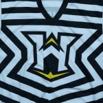 A close-up of a black and white striped jersey featuring a stylized white letter W logo with yellow accents in the center.