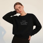 A young woman wearing a black crewneck sweatshirt with the white cursive text Infinite Echoes. Endless Possibilities printed on the chest.