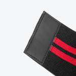 Close-up of a black elastic wrist or knee wrap with two red stripes and a stitched black rectangular patch at the end, set against a white background.