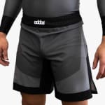 A close-up of a person wearing gray and black athletic training shorts with a black waistband featuring the white addos logo.