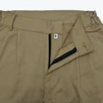 Close-up of the waistband and fly of beige khaki trousers, showing the button, partially open zipper, size M tag, and elastic waist details.