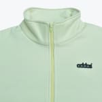 Close-up of a pale green mock neck zip-up sweatshirt featuring a black addos logo on the chest.