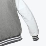 Close-up of a varsity jacket with a grey wool body, white leather sleeve, and grey and white striped ribbed cuffs.