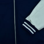 Close-up of a navy blue varsity jacket with a silver zipper, a white sleeve, and a striped ribbed cuff.
