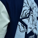 Close-up of a navy blue varsity jacket with a cream sleeve, featuring a large star-shaped patch embroidered with a detailed roaring tiger illustration.