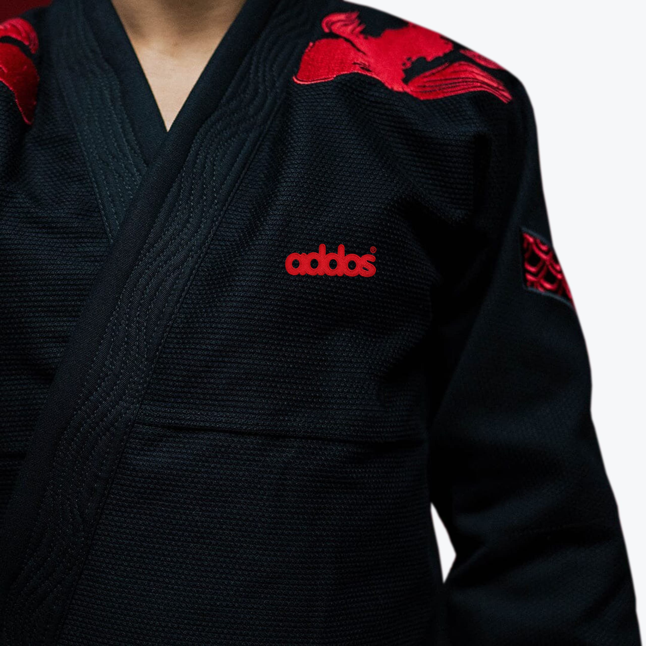 Close-up of a black martial arts gi jacket with red koi fish embroidery on the shoulders and a red addos logo on the chest.
