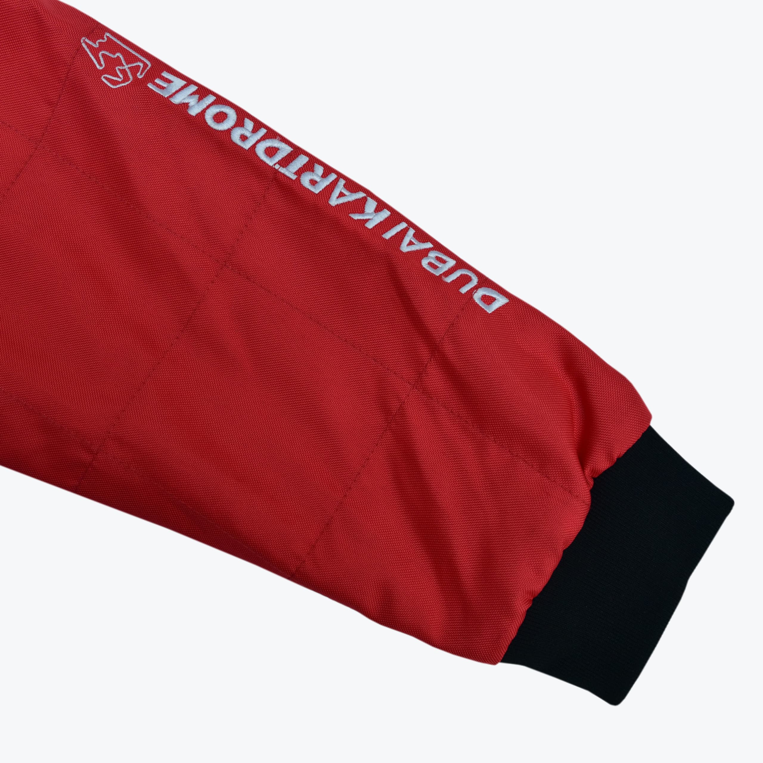 A close-up view of a red quilted jacket sleeve featuring the white embroidered text DUBAI KARTDROME and a black cuff.