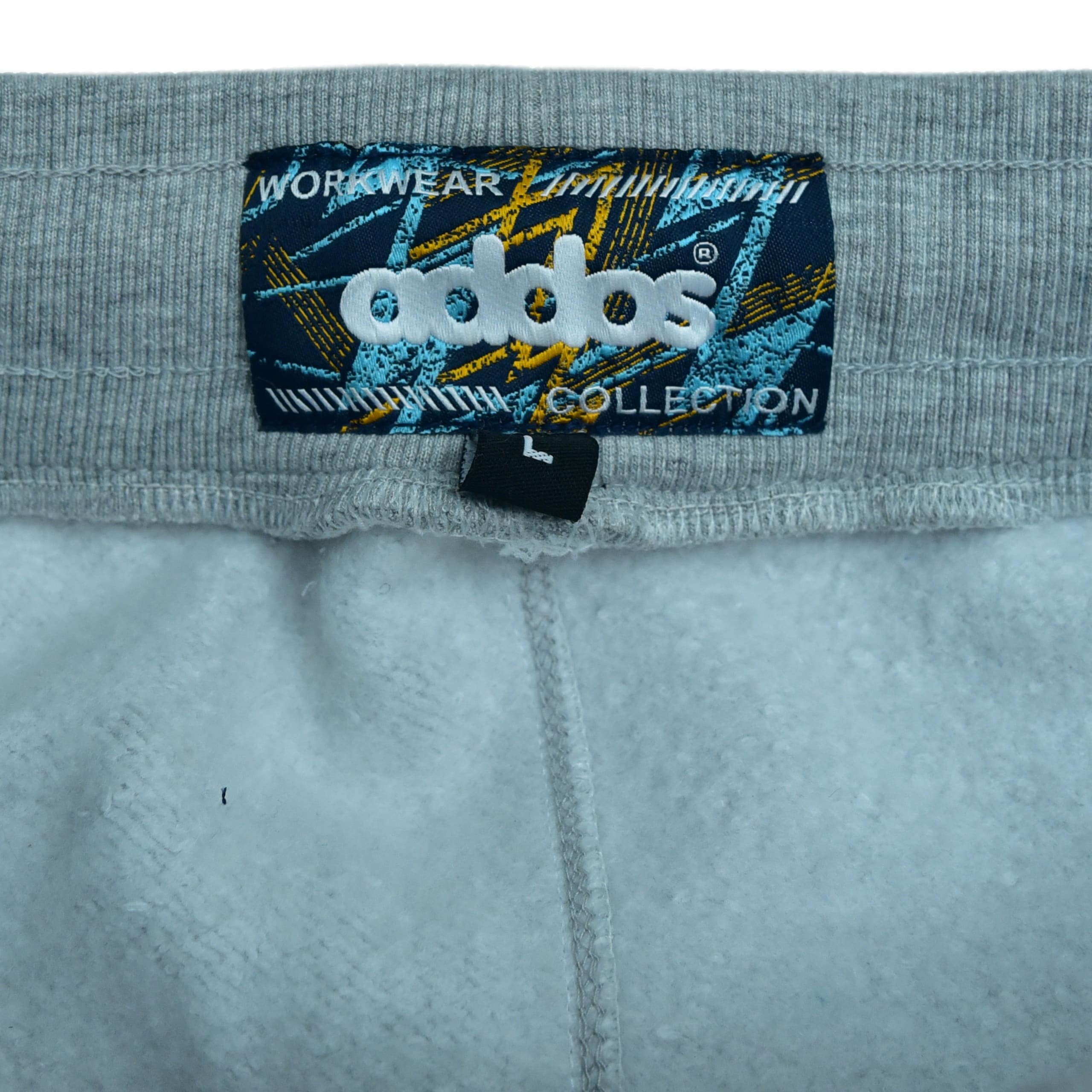 Close-up of a rectangular Addos Workwear Collection label on a grey ribbed waistband, showing white embroidered branding and a small black size L tag.