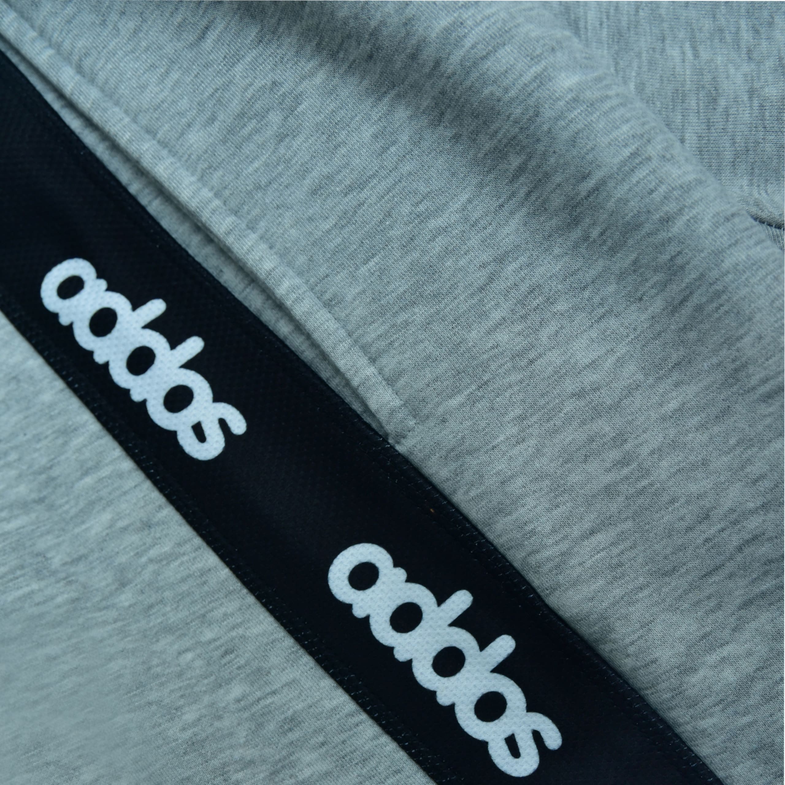 Close-up of grey heathered fabric with a diagonal black stripe featuring the white Addos logo printed repeatedly.