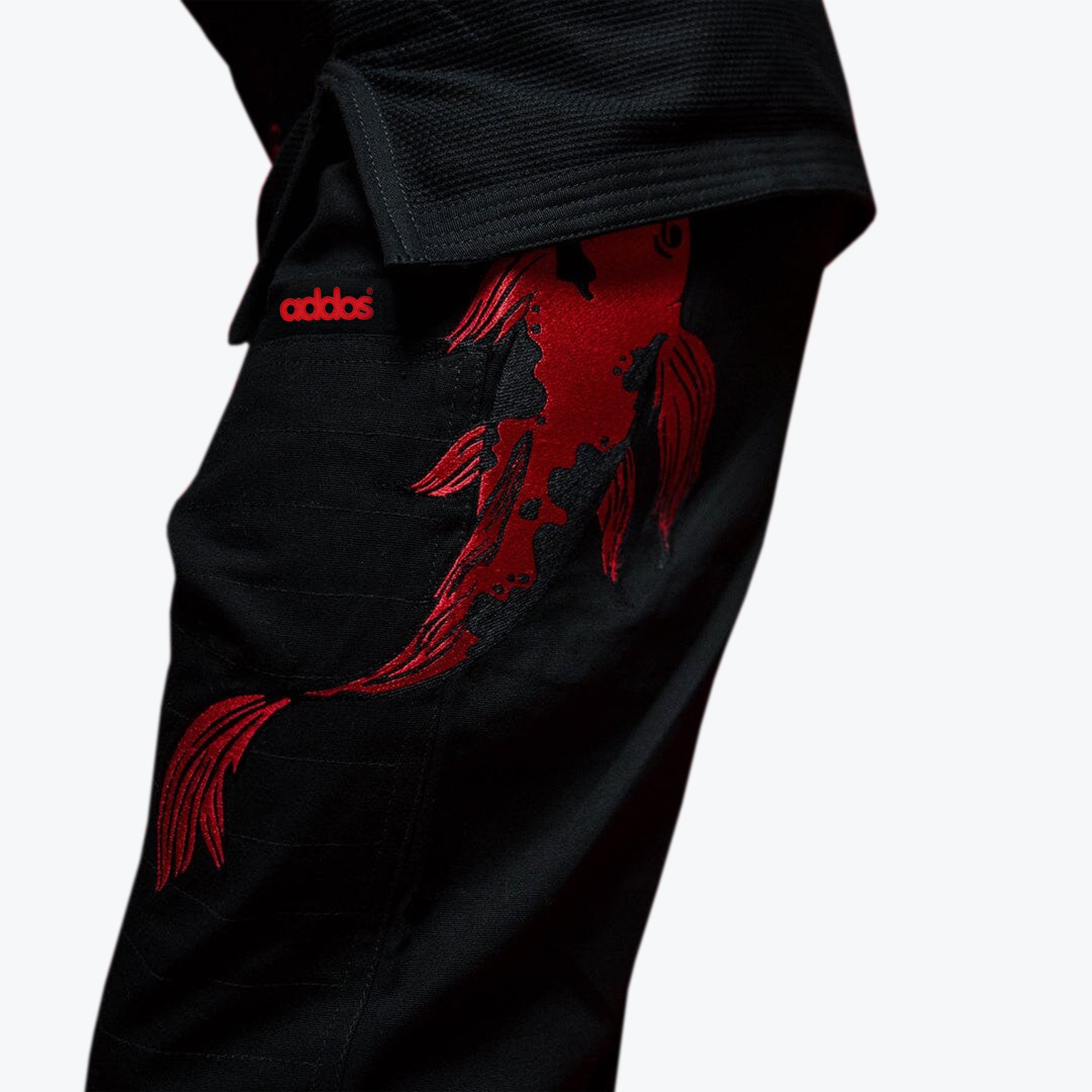 Close-up of black Addos BJJ gi pants featuring a large, detailed red embroidered koi fish on the thigh.