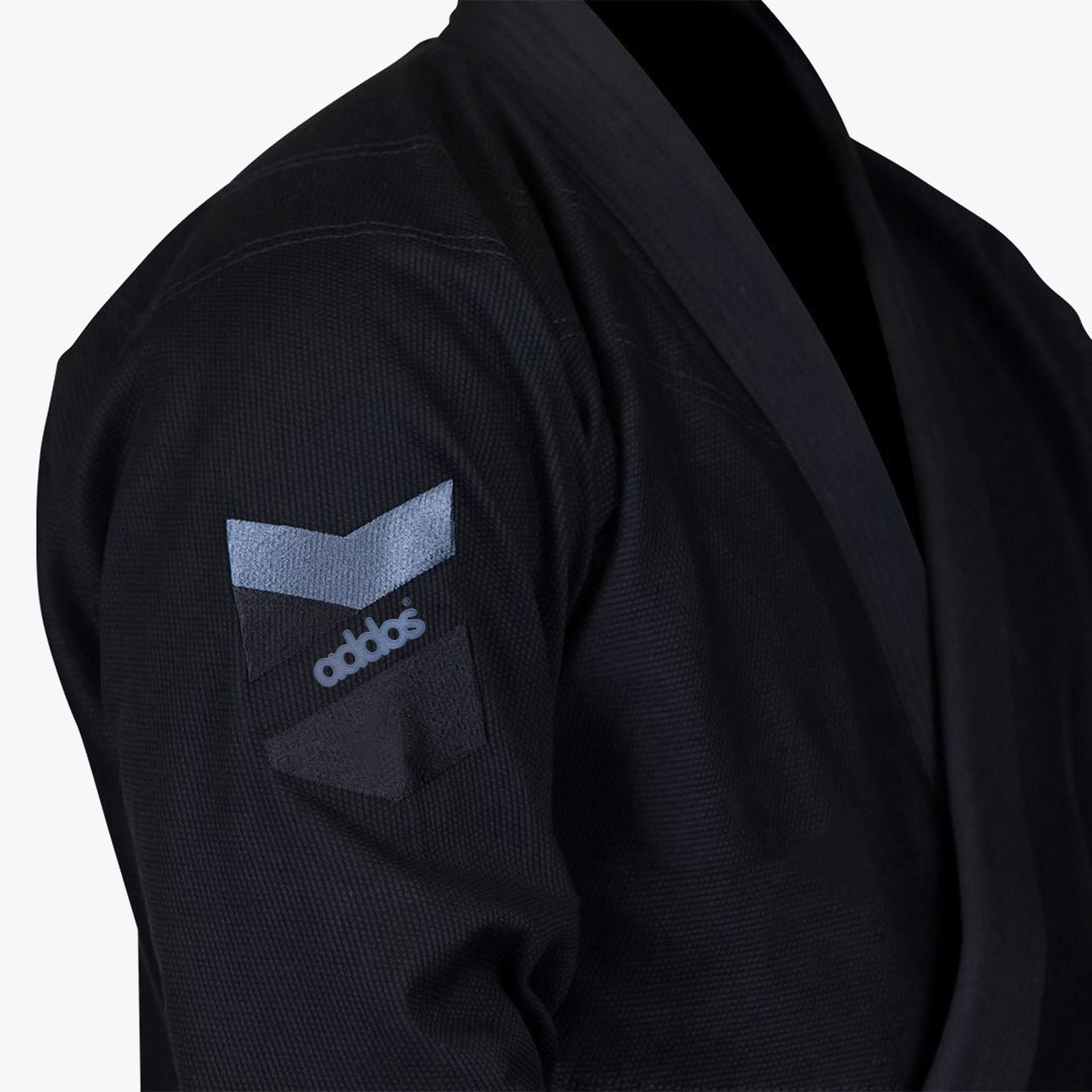 Close-up of the sleeve of a black Addos Jiu-Jitsu gi featuring a grey and black brand logo patch on the upper arm.