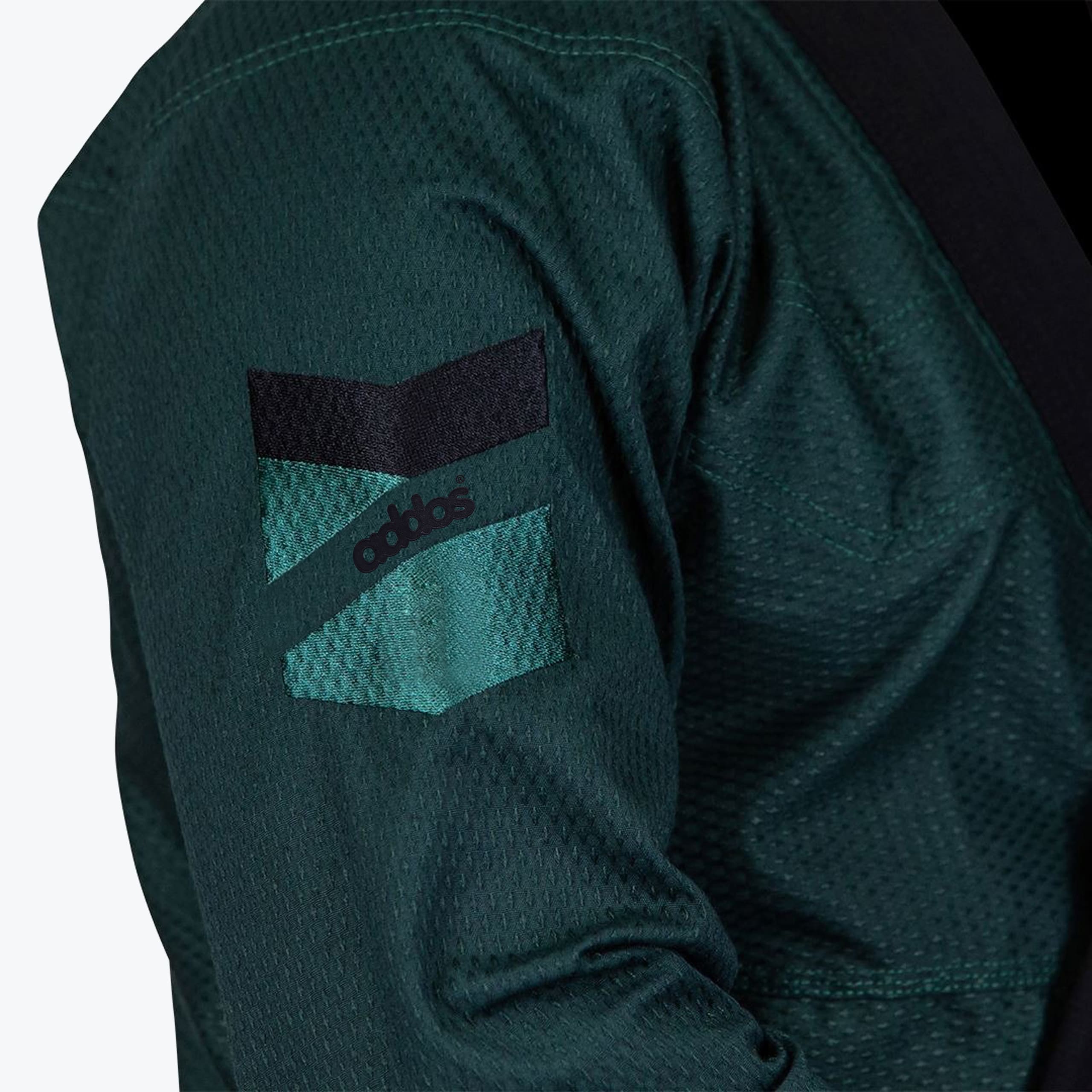 Close-up of a dark green textured Jiu-Jitsu gi sleeve with an embroidered Addos logo patch.