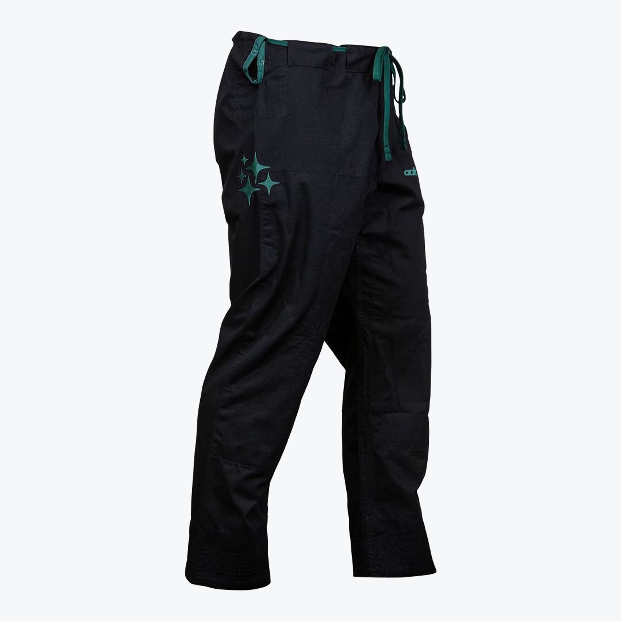 A side-angle view of black martial arts gi pants with a green drawstring and green star embroidery on the thigh, set against a white background.