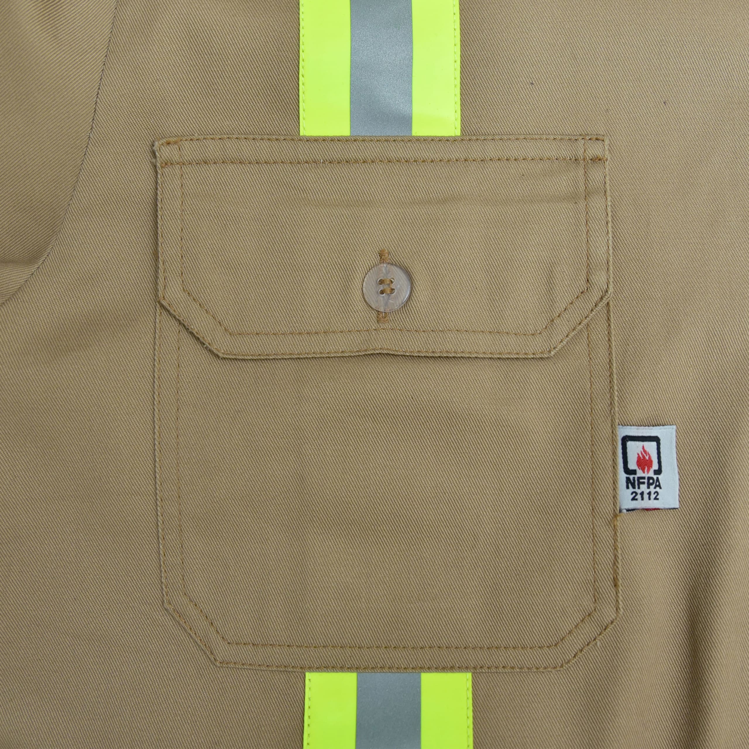 Close-up of a khaki work shirt pocket with a buttoned flap, a vertical yellow and silver reflective safety stripe, and an NFPA 2112 flame-resistant label.