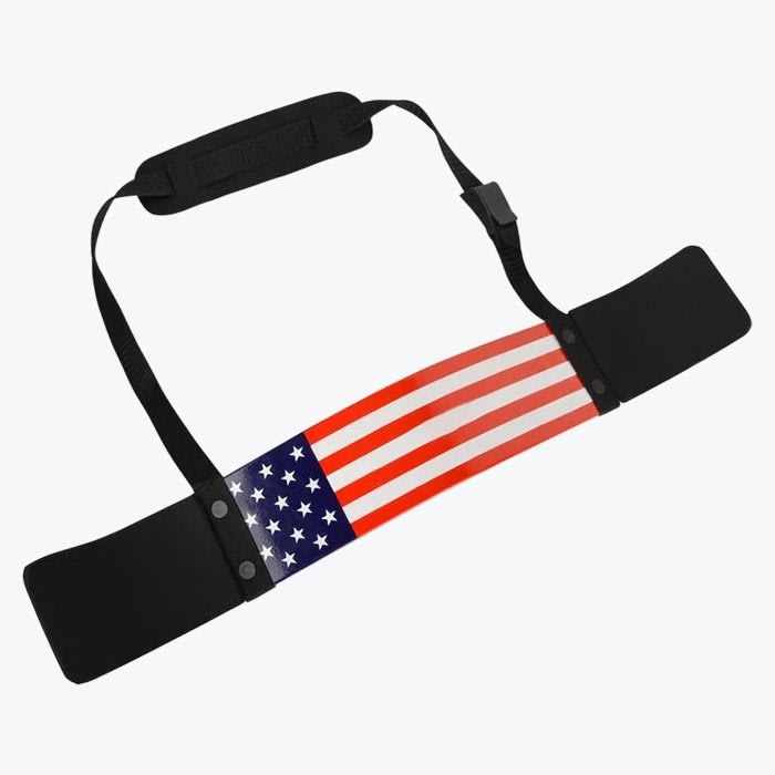 An arm blaster for bicep curls featuring an American flag design on the main curved plate, black padded elbow rests, and an adjustable neck strap with a padded neck guard.