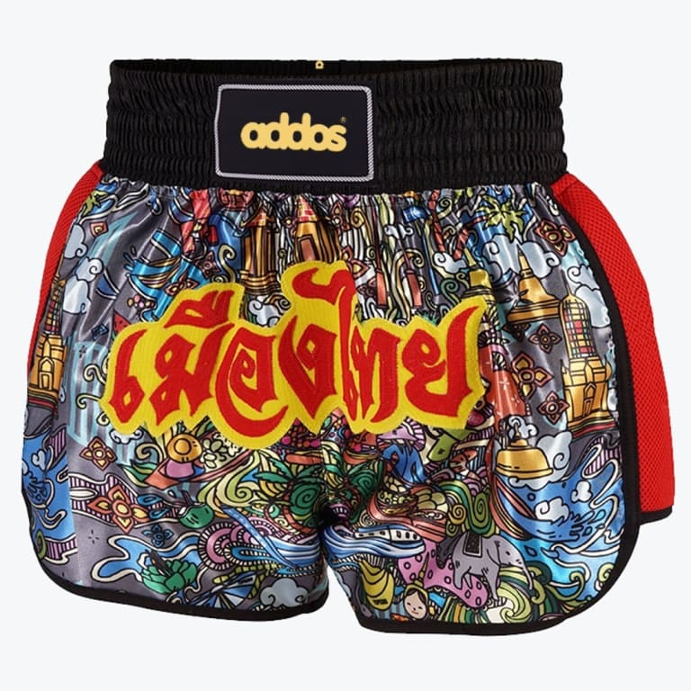 A pair of Muay Thai shorts with a colorful doodle pattern of Thai culture, a black elastic waistband with an addos patch, and large red and yellow Thai script on the front.