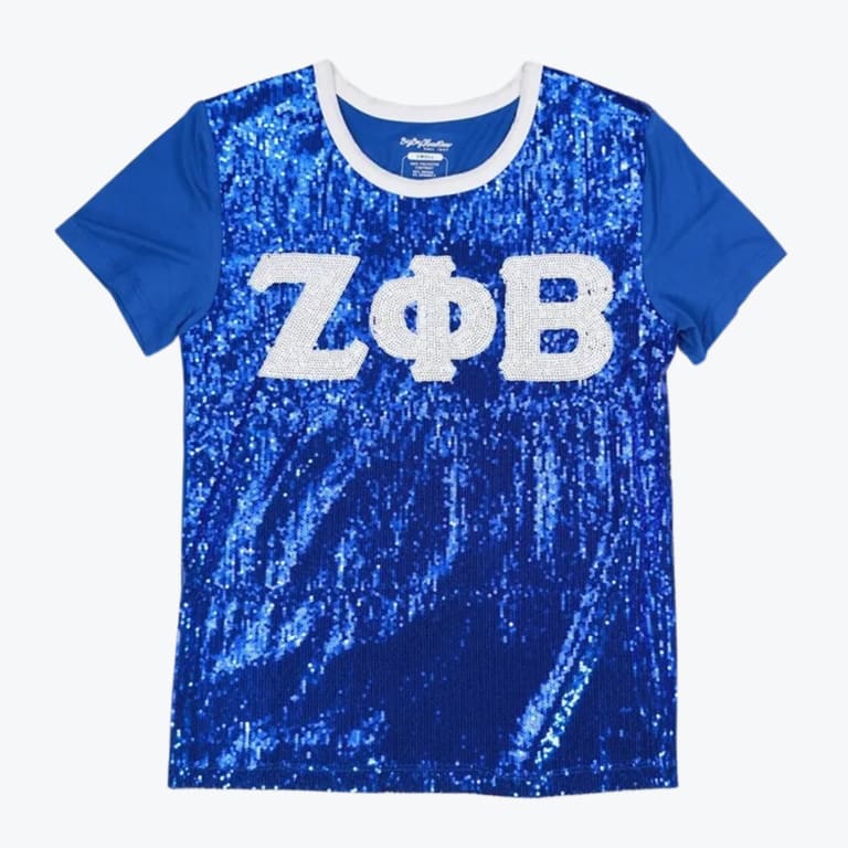 A royal blue t-shirt with a shiny sequined front, featuring the Greek letters Z, Phi, and B in white sequins across the chest.
