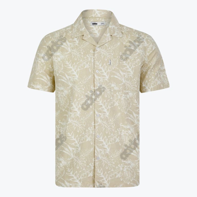 A mens light beige short sleeve button up shirt with a white tropical leaf pattern featuring a camp collar and a chest pocket displayed against a plain white background