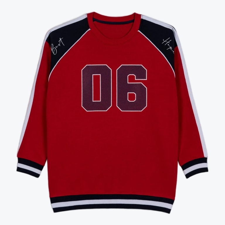 A red long-sleeve sweatshirt with a large graphic on the front, navy shoulder panels with script text, and striped cuffs.