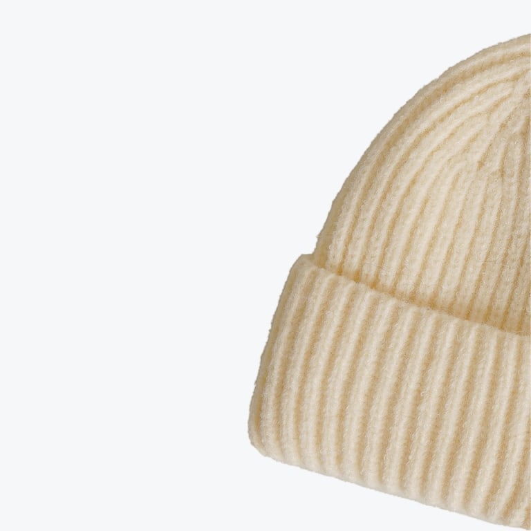 Close-up of a cream-colored ribbed knit beanie hat with a folded brim on a white background.