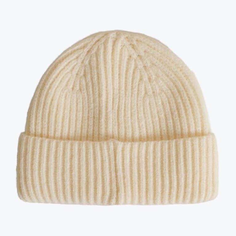 A cream-colored ribbed knit beanie hat with a folded cuff, isolated on a plain white background.