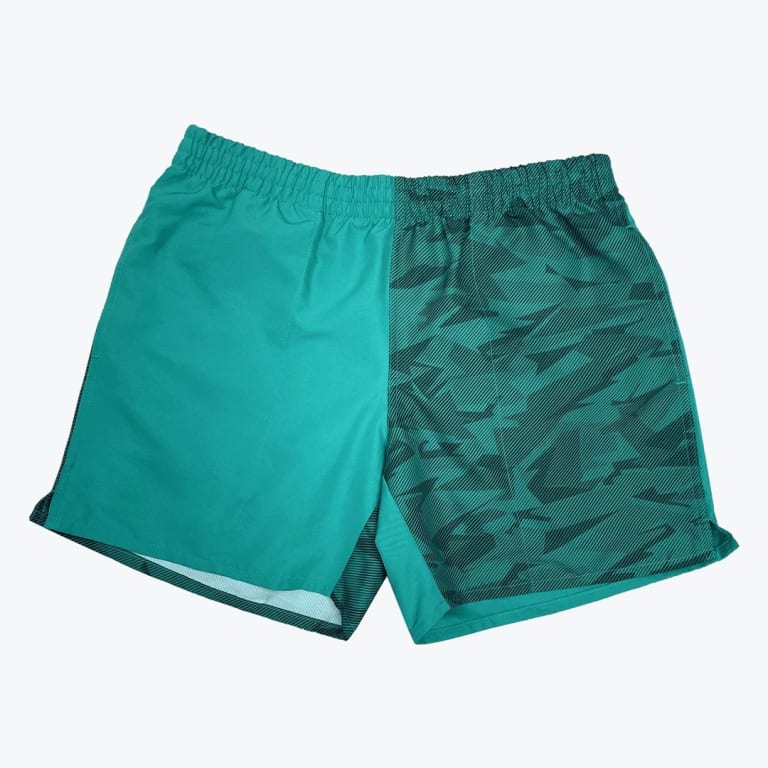 A pair of teal athletic shorts with a split design, showing a solid teal fabric on one side and a dark teal geometric patterned fabric on the other, set against a plain white background.