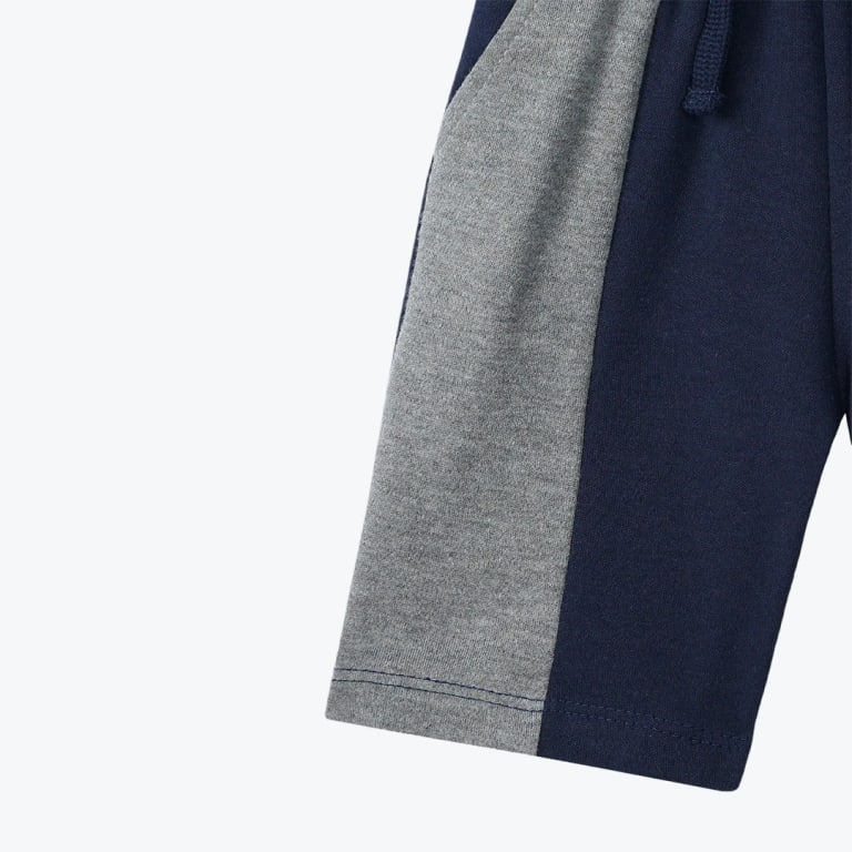 Close-up of navy blue shorts featuring a contrasting grey side panel and a drawstring waist against a white background.