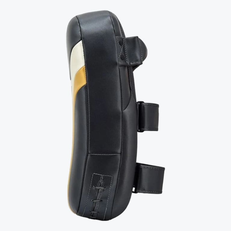 Side profile of a black leather Muay Thai kick pad with a curved design, a top handle, and two forearm straps on a white background.