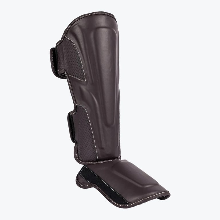 A dark brown leather shin and instep guard with white stitching, displayed against a solid white background.