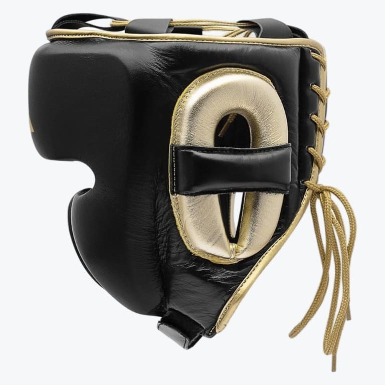 A side-profile view of a black leather boxing headguard with metallic gold padding around the ear, gold trim, and gold laces, set against a plain white background.